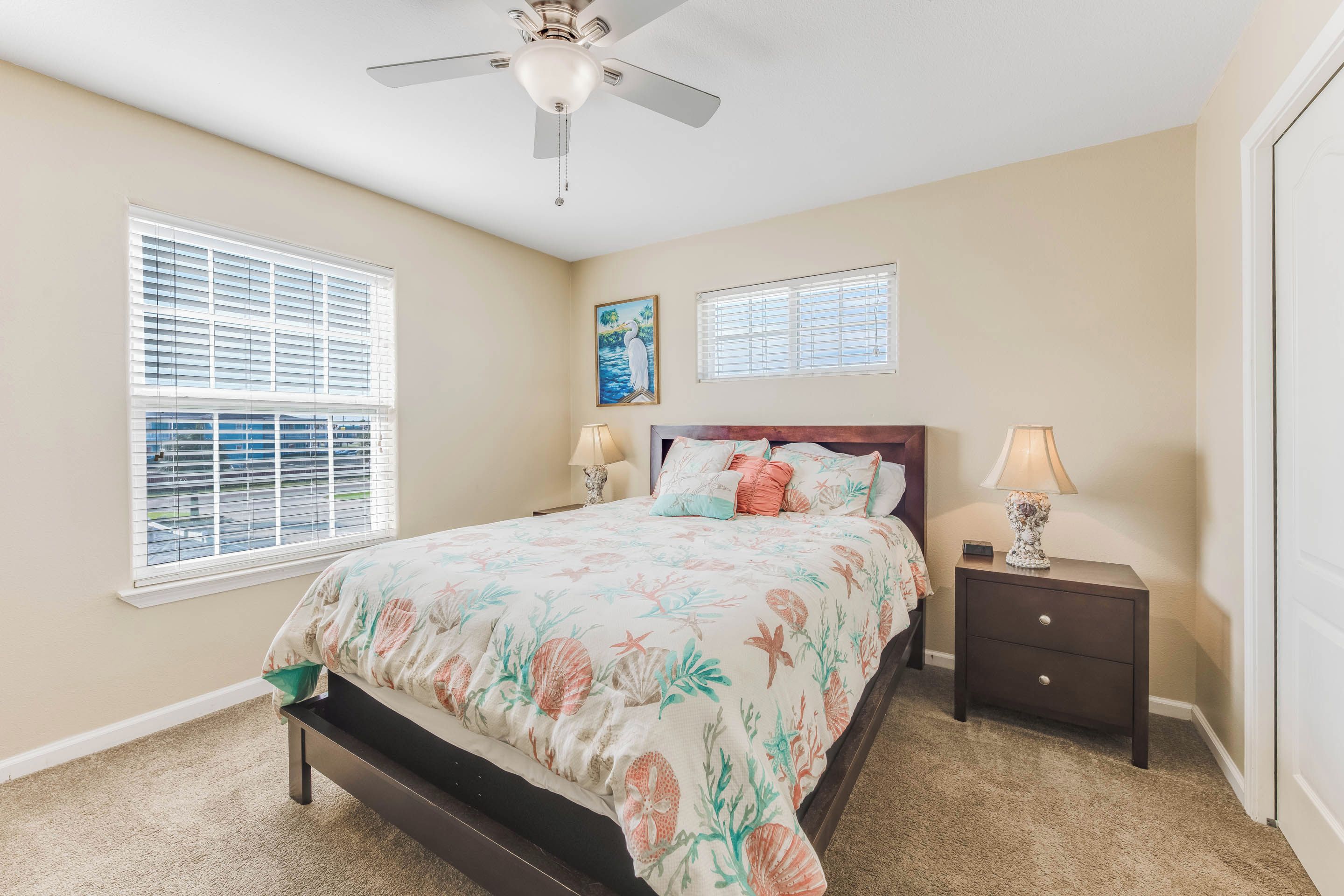 A bedroom with a bed, two nightstands, a ceiling fan, and two windows with blinds.
