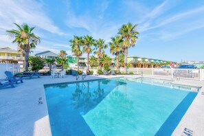 A swimming pool with lounge chairs and palm trees, surrounded by houses. - Pop-A-Top by Silver Sands Vacation Rentals (Port Aransas)