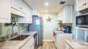 A kitchen with white cabinets, a stainless steel refrigerator, a microwave, and a wooden floor. - Pearl Marlin by Silver Sands Vacation Rentals (Port Aransas)