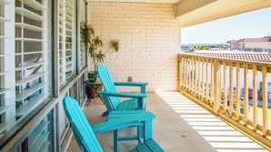 A balcony with two turquoise Adirondack chairs, a potted plant, and a view of neighboring buildings. - Pearl Marlin by Silver Sands Vacation Rentals (Port Aransas)