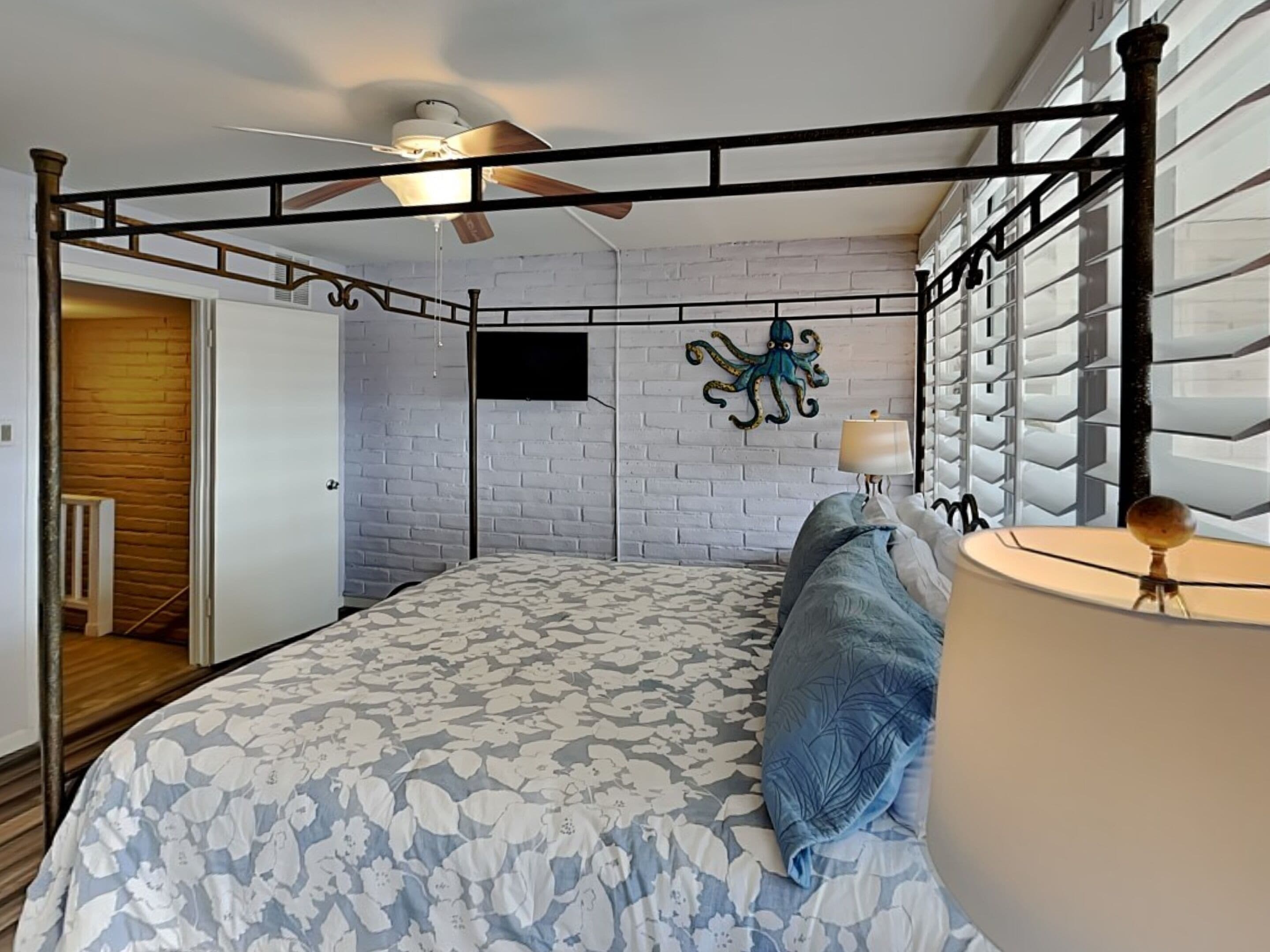 A bedroom with a four-poster bed, a ceiling fan, a brick-patterned wall, and a decorative octopus wall art piece.