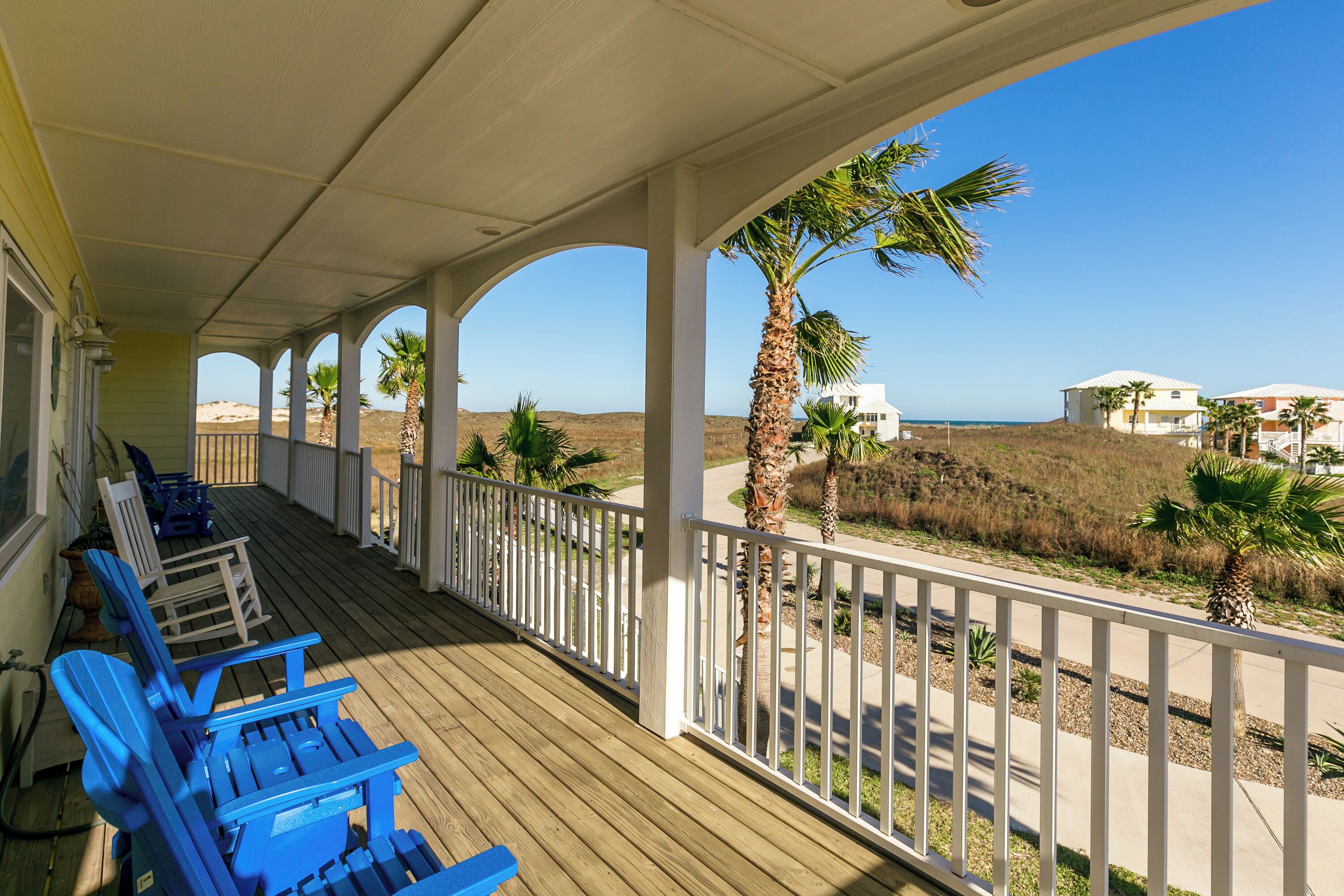 Eine überdachte Veranda mit blauen Stühlen und Blick auf den Strand.