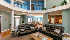 A spacious living area with leather sofas, a wooden coffee table, and a high ceiling with a balcony. - Porpoise of Life by Silver Sands Vacation Rentals (Port Aransas)