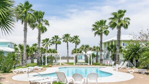 A pool area with white lounge chairs, palm trees, and a gazebo. - Porpoise of Life by Silver Sands Vacation Rentals (Port Aransas)