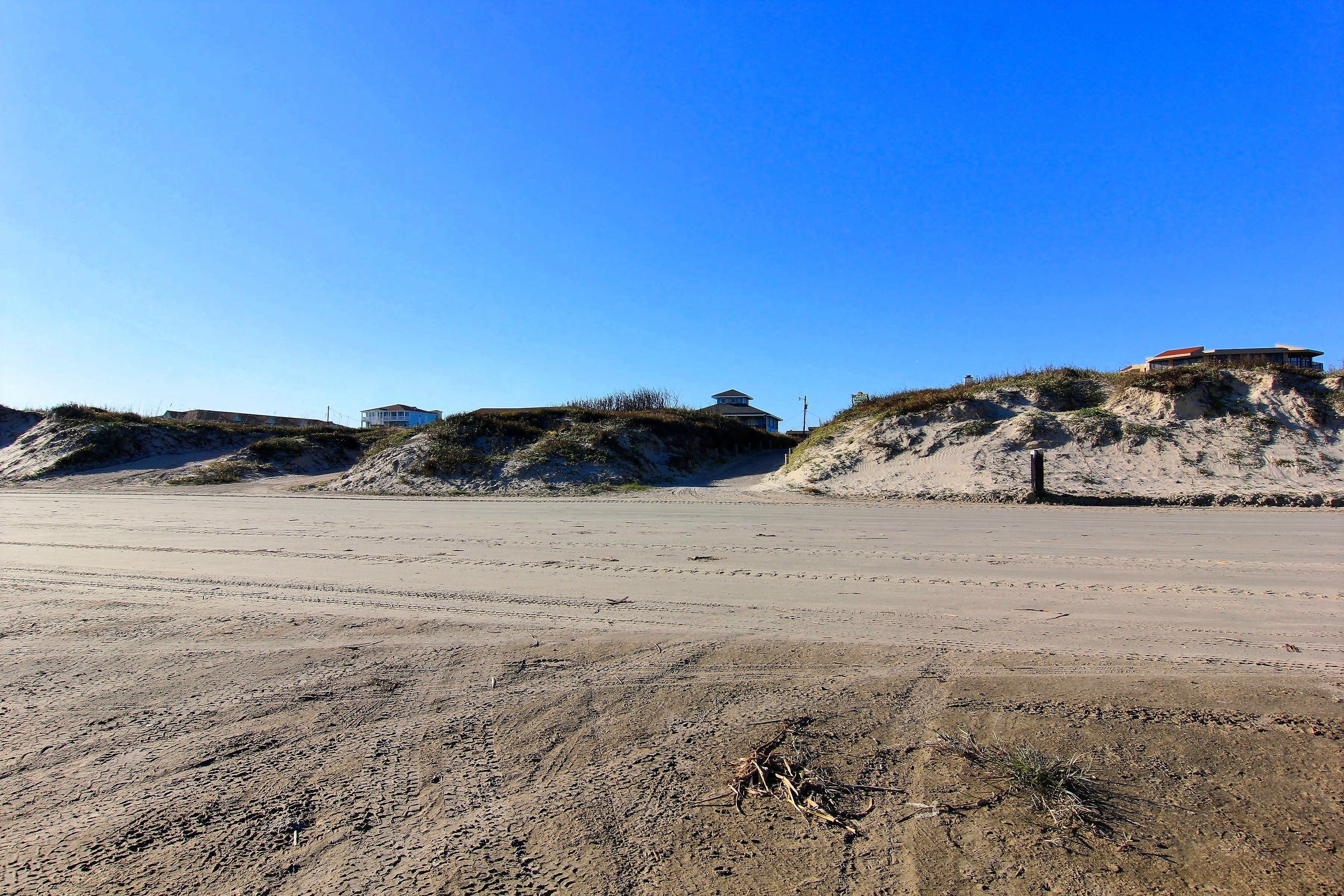 Ein Sandstrand mit Dünen und einigen Gebäuden darauf.