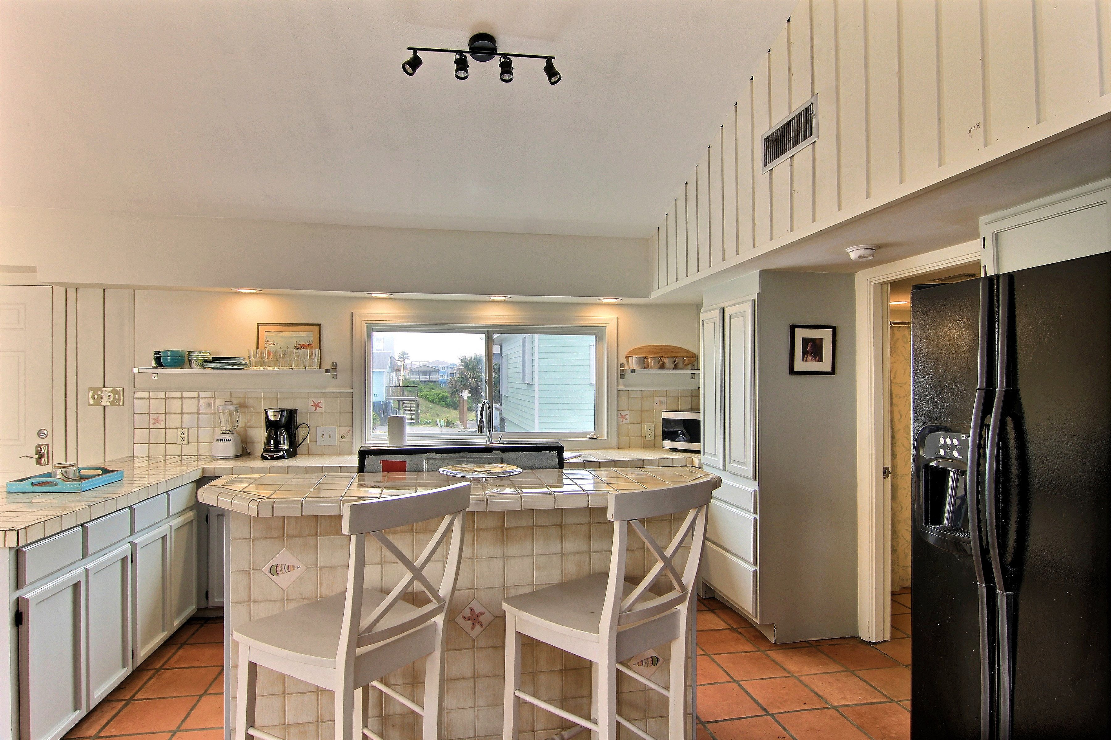 A kitchen with a bar area, white cabinets, a black refrigerator, and a window with a view of the outside.
