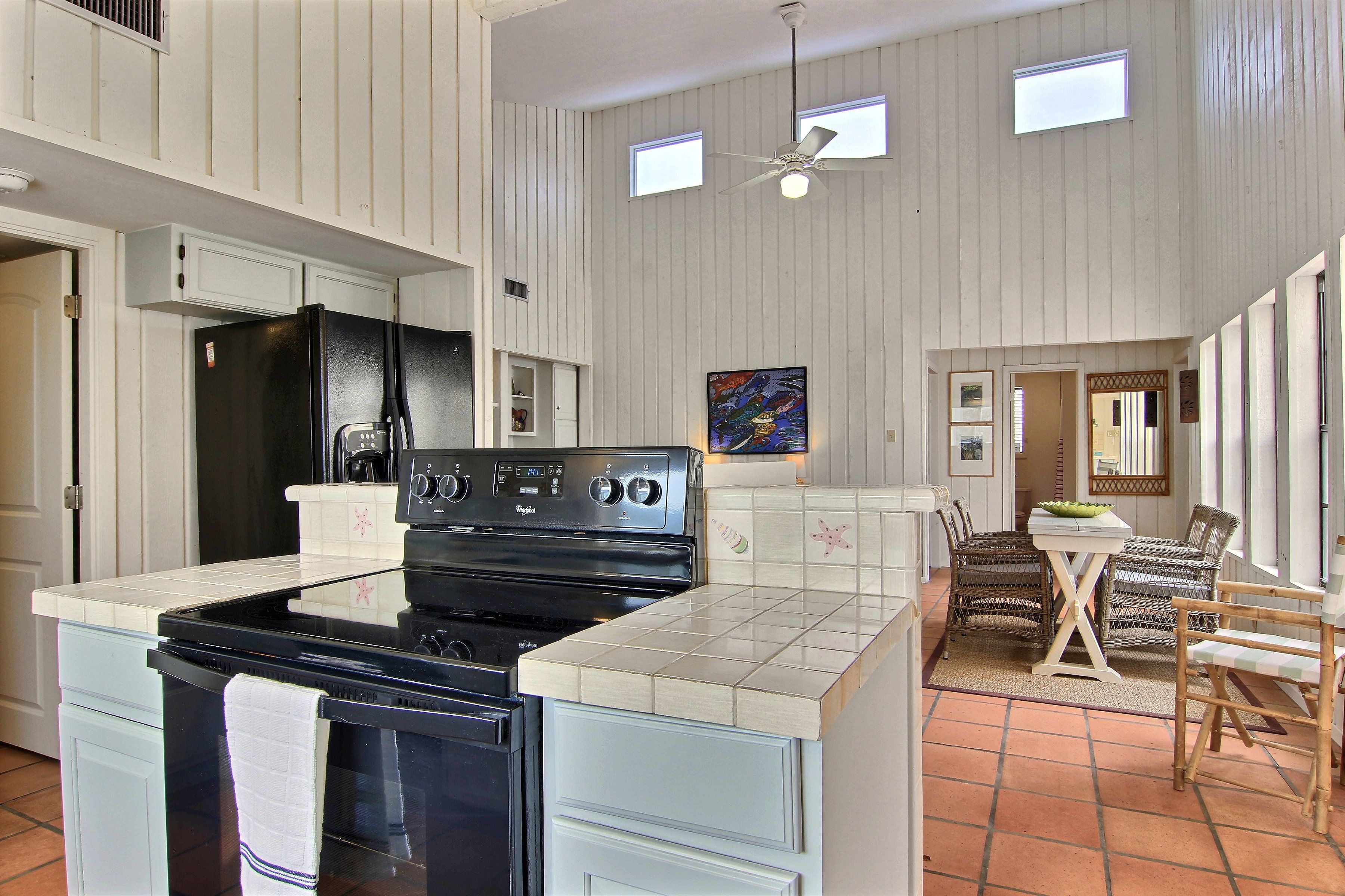 A kitchen with a black stove, white cabinets, and a dining area with wicker chairs and a table.