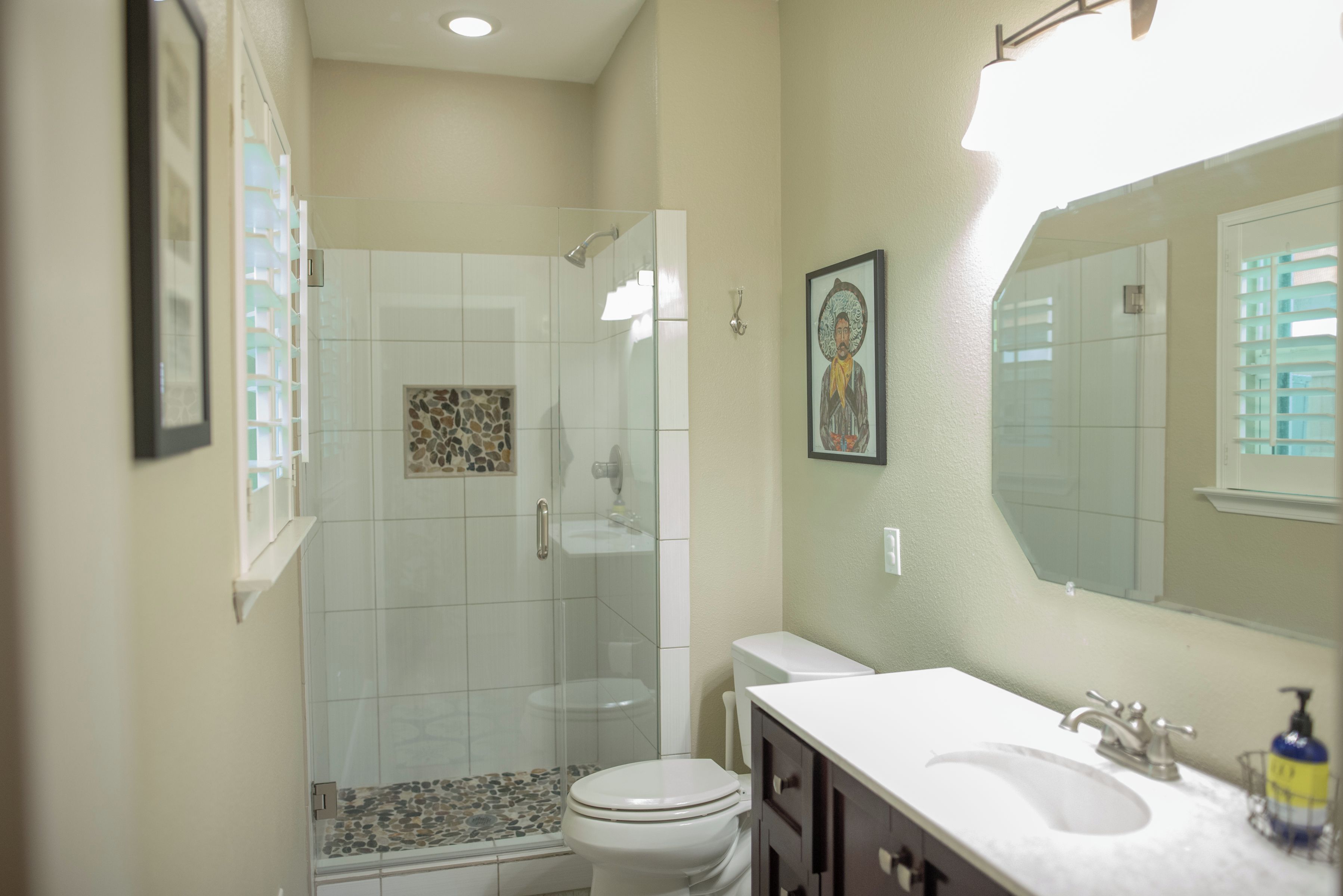A bathroom with a glass-enclosed shower, a toilet, a sink, and a mirror.
