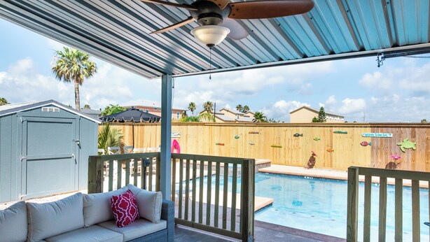 An outdoor pool area with a covered patio, a wooden fence, and a small shed. - Port A Ponderosa by Silver Sands Vacation Rentals (Port Aransas)