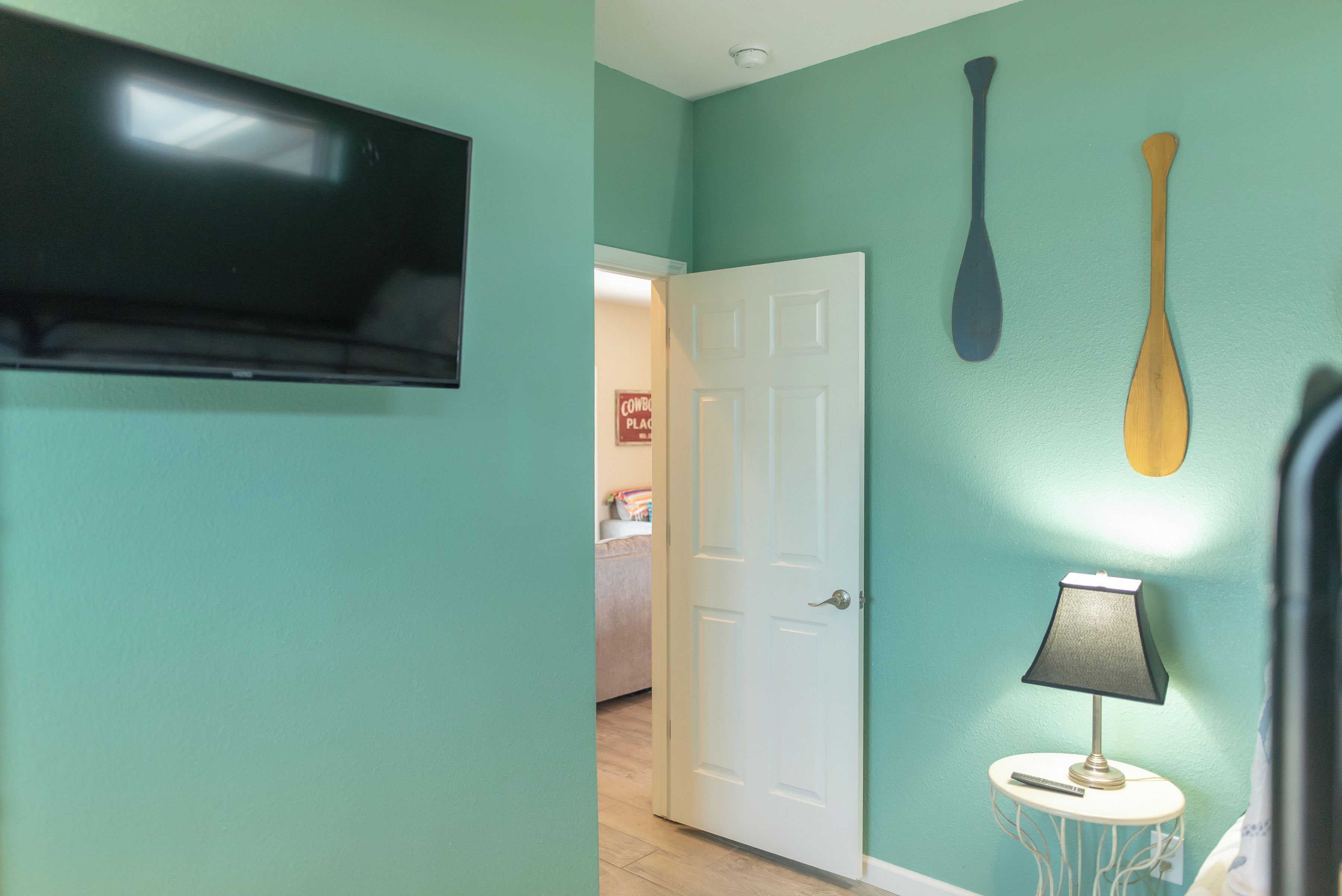 Een gang met blauwgroene wanden, een witte deur, een bevestigde televisie en twee decoraties in de vorm van peddels.