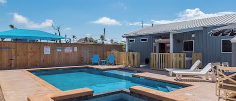 A swimming pool with a wooden deck, lounge chairs, and a covered area.