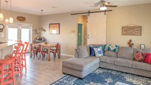A spacious living room with a large grey sectional sofa, a dining area with wooden chairs, and a kitchen with a bar counter. - Port A Ponderosa by Silver Sands Vacation Rentals (Port Aransas)