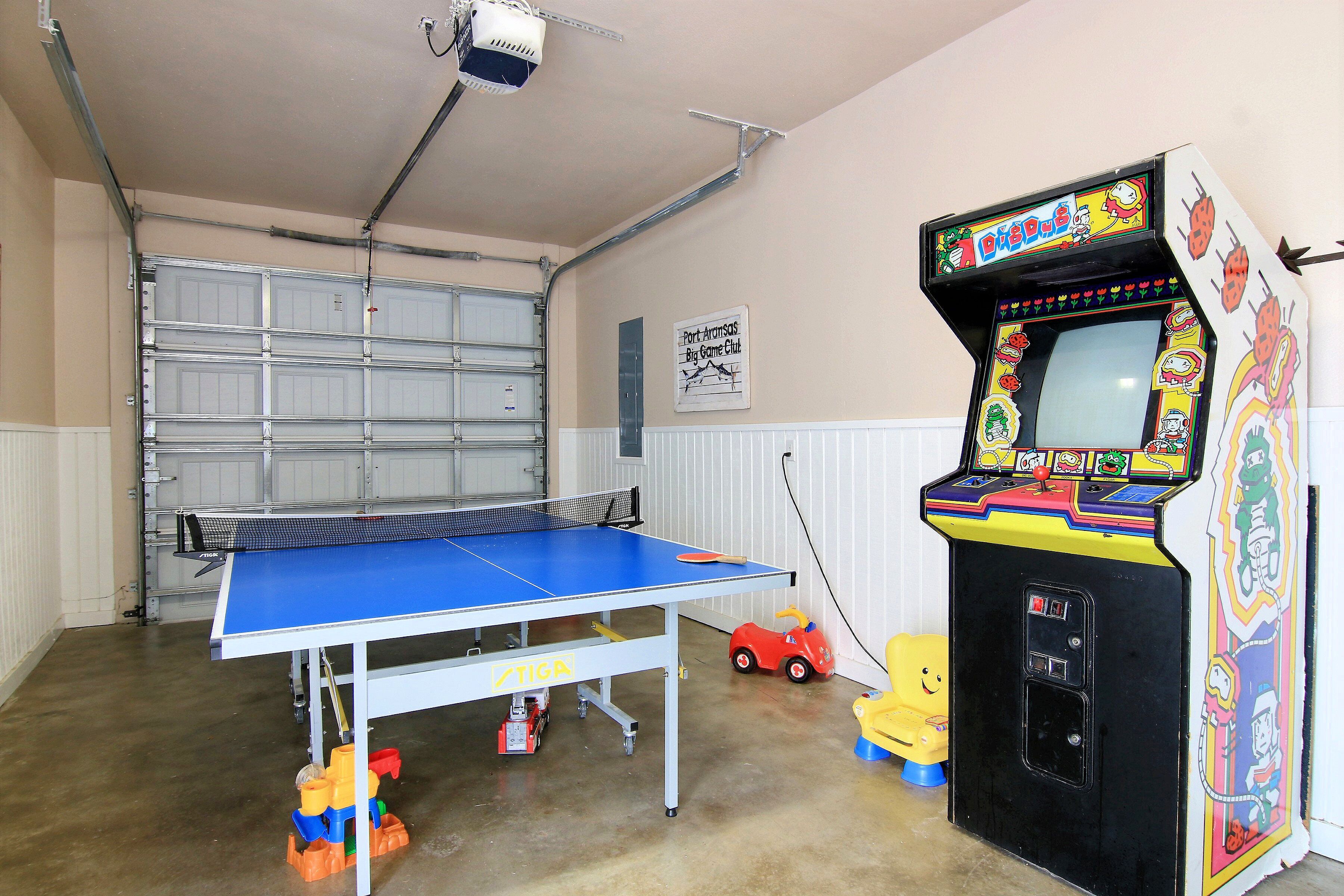 A garage with a ping pong table, a children's ride-on toy car, and a colorful arcade machine.
