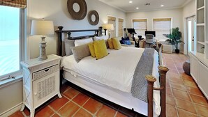 A spacious bedroom with a large bed, a ceiling fan, and a view of the beach.
