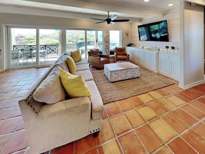 A spacious living room with a large sofa, a television mounted on the wall, and a ceiling fan. - Salt and Horns by Silver Sands Vacation Rentals (Port Aransas)