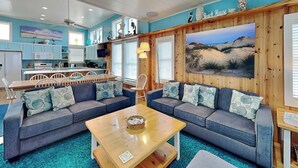 A cozy living room with a large sectional sofa, a wooden coffee table, and a kitchen area in the background. - Port A Paradise by Silver Sands Vacation Rentals (Port Aransas)