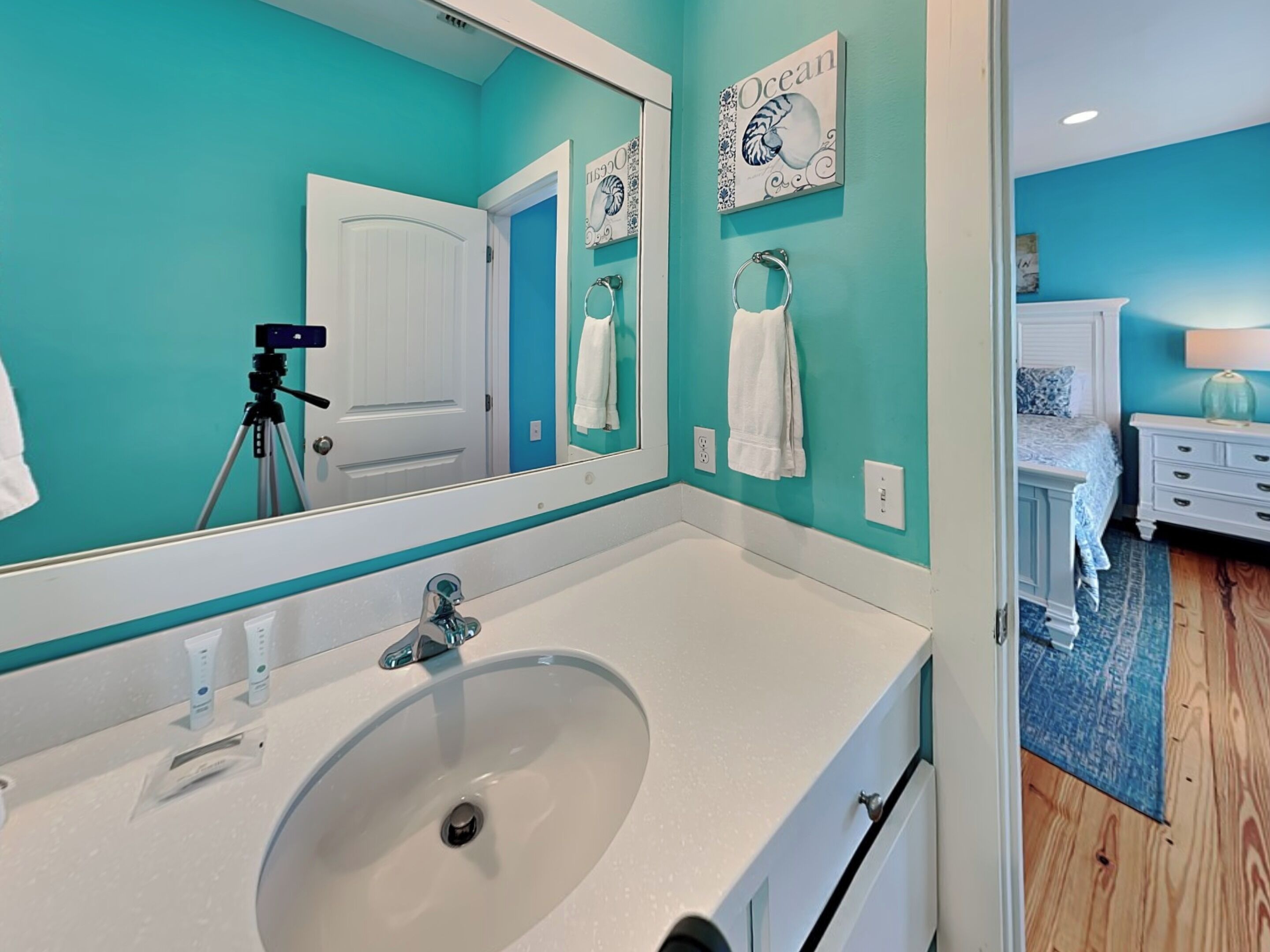 Un bagno con uno specchio grande, un lavabo e una porta. Asciugamani appesi al muro e una videocamera su un cavalletto.