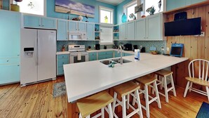 A modern kitchen with a large island, wooden bar stools, and a built-in TV. - Port A Paradise by Silver Sands Vacation Rentals (Port Aransas)