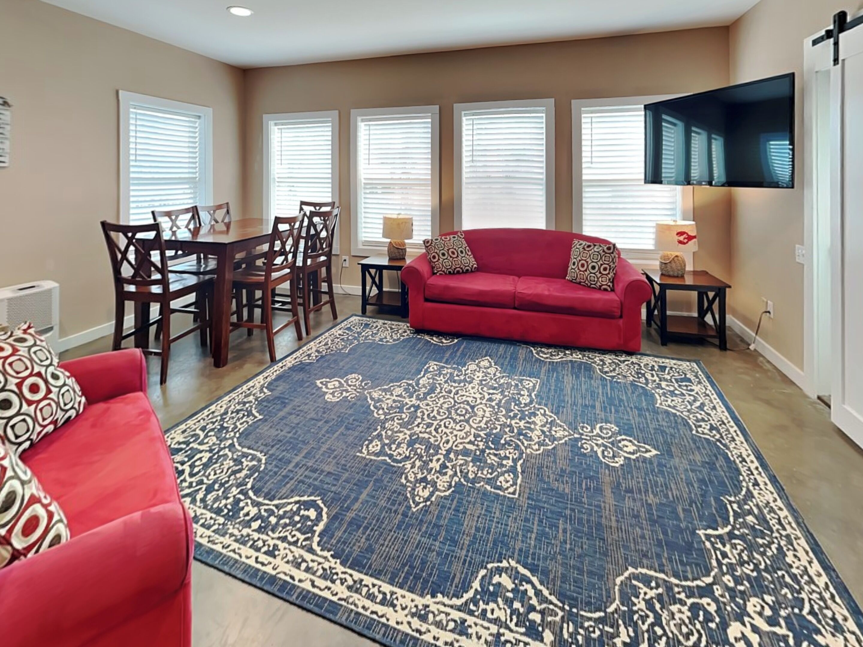 A living room with a red sofa, a matching armchair, a dining table with chairs, and a large patterned rug.