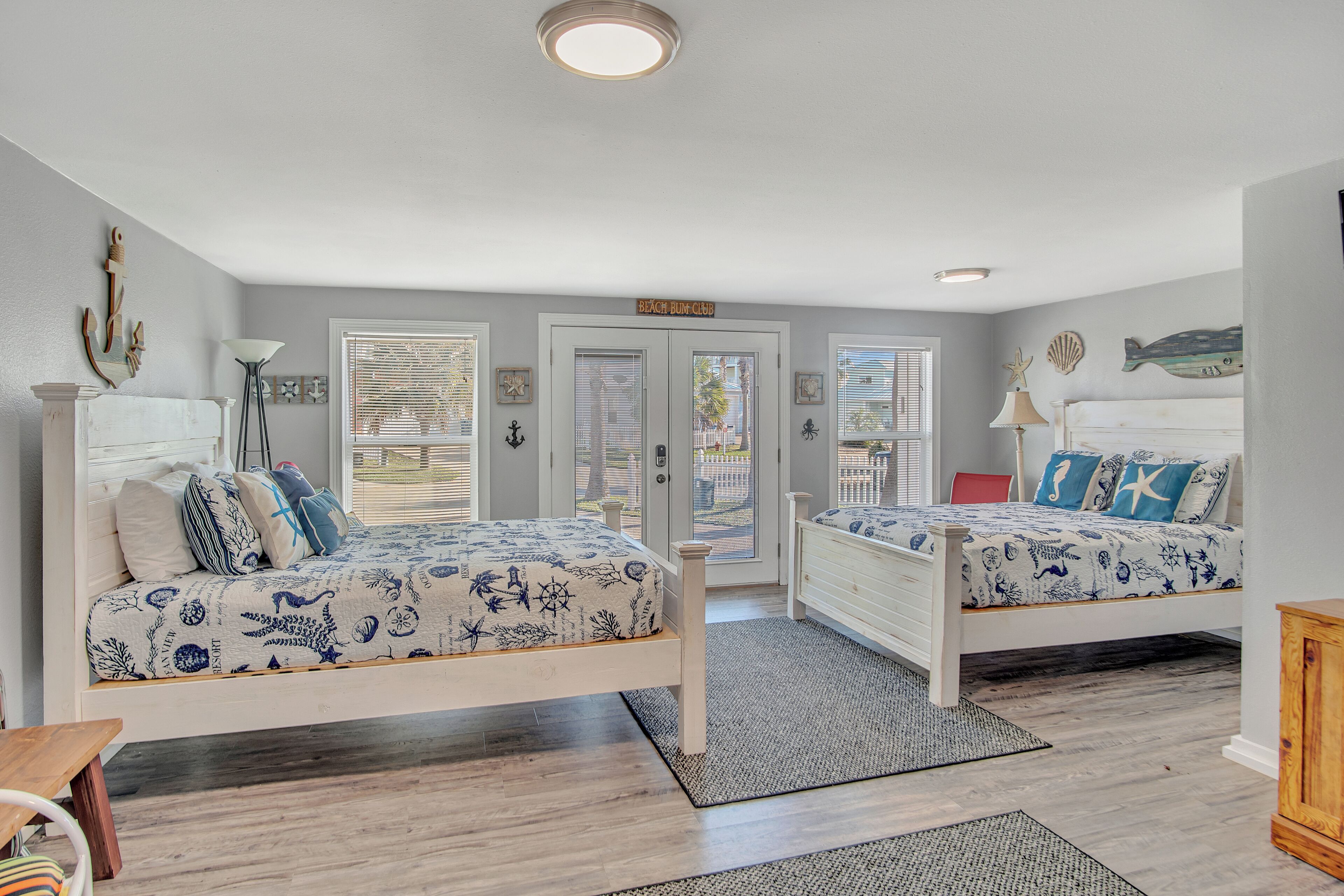 A bedroom with two beds, a wooden floor, and a view of the outside through a door.