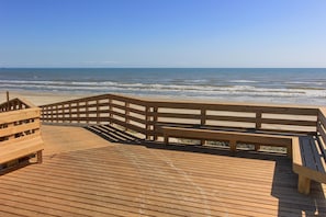 A wooden boardwalk leading to a beach with a wooden railing and benches.