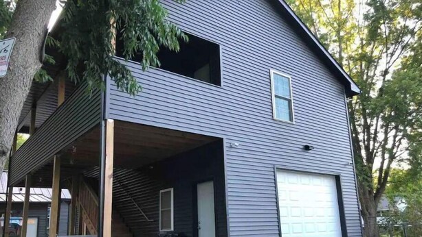 Ein zweigeschossiges Haus mit Garage, einer überdachten Veranda und einer Treppe, die zum oberen Stock führt.