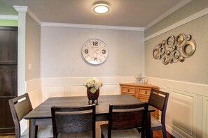 Uma sala de jantar com mesa de madeira, quatro cadeiras, um relógio de parede e arte decorativa.