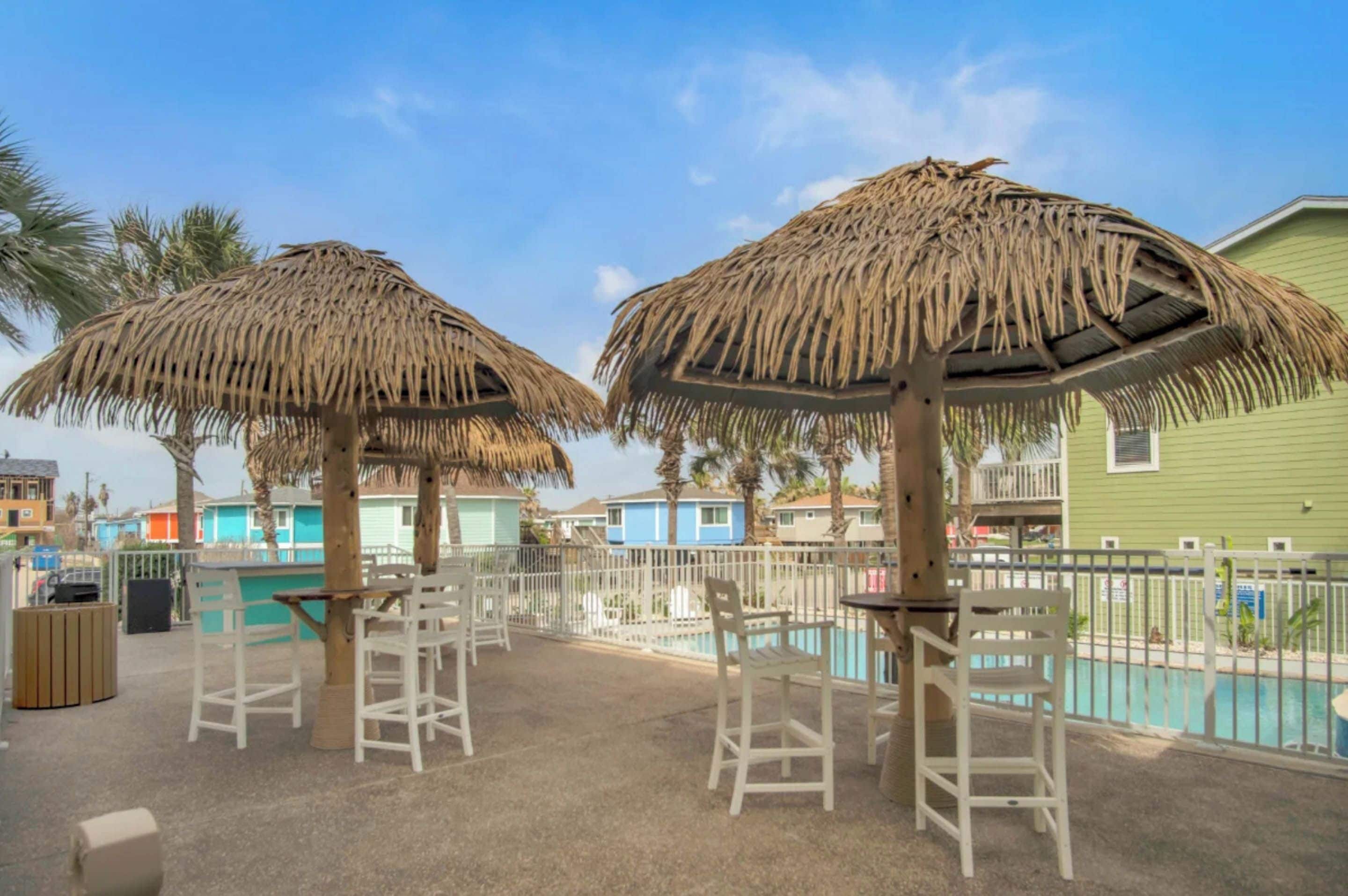 A poolside area with thatched umbrellas, white plastic chairs, and a pool.