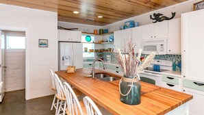 A modern kitchen with wooden countertops, white cabinets, and a central island with bar stools. - Sea La Vie by Silver Sands Vacation Rentals (Port Aransas)