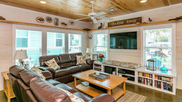 A cozy living room with a brown leather sofa, a wooden coffee table, and a bookshelf filled with books. - Sea La Vie by Silver Sands Vacation Rentals (Port Aransas)