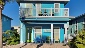 A two-story building with a balcony, a green door, and a small porch area with chairs. - Sea La Vie by Silver Sands Vacation Rentals (Port Aransas)