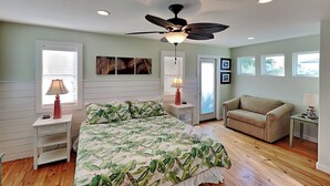A bedroom with a bed, a ceiling fan, a nightstand, a lamp, a couch, and a window. - Sea La Vie by Silver Sands Vacation Rentals (Port Aransas)