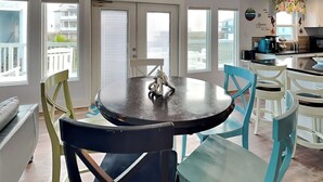 A dining area with a round table and chairs, a kitchen in the background, and large windows with a view of the outside. - Sea View Villa by Silver Sands Vacation Rentals (Port Aransas)