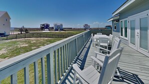 A wooden deck with white chairs, a railing, and a view of buildings in the distance. - Sea View Villa by Silver Sands Vacation Rentals (Port Aransas)