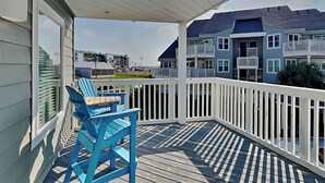 Une véranda couverte avec deux fauteuils Adirondack bleus, une balustrade blanche et une vue sur des immeubles à plusieurs étages en arrière-plan.