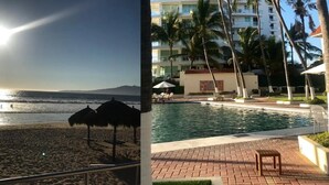 A beach with a flag, a pool area with lounge chairs, and a building with balconies and palm trees. - Costa Vallarta by TRVL2HM (Nuevo Nayarit)