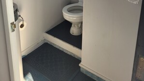 Een kleine, smalle badkamer met toilet, een raam en een handdoek aan de muur.