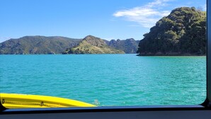 Uitzicht vanaf een boot, met een gele kajak op de voorgrond, kalm turquoise water en groene heuvels op de achtergrond.