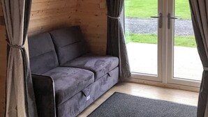 Une pièce avec un canapé gris, des murs en bois et une porte-fenêtre coulissante donnant sur un espace extérieur verdoyant.