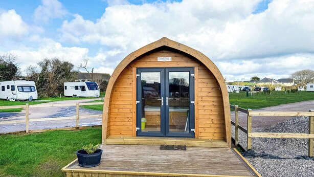 Une structure en bois avec une porte en verre, une enseigne au-dessus de la porte et un petit espace de porche agrémenté d’une plante en pot.