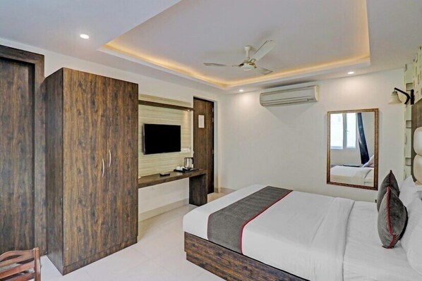 A hotel room with a bed, a TV, a ceiling fan, and a mirror.