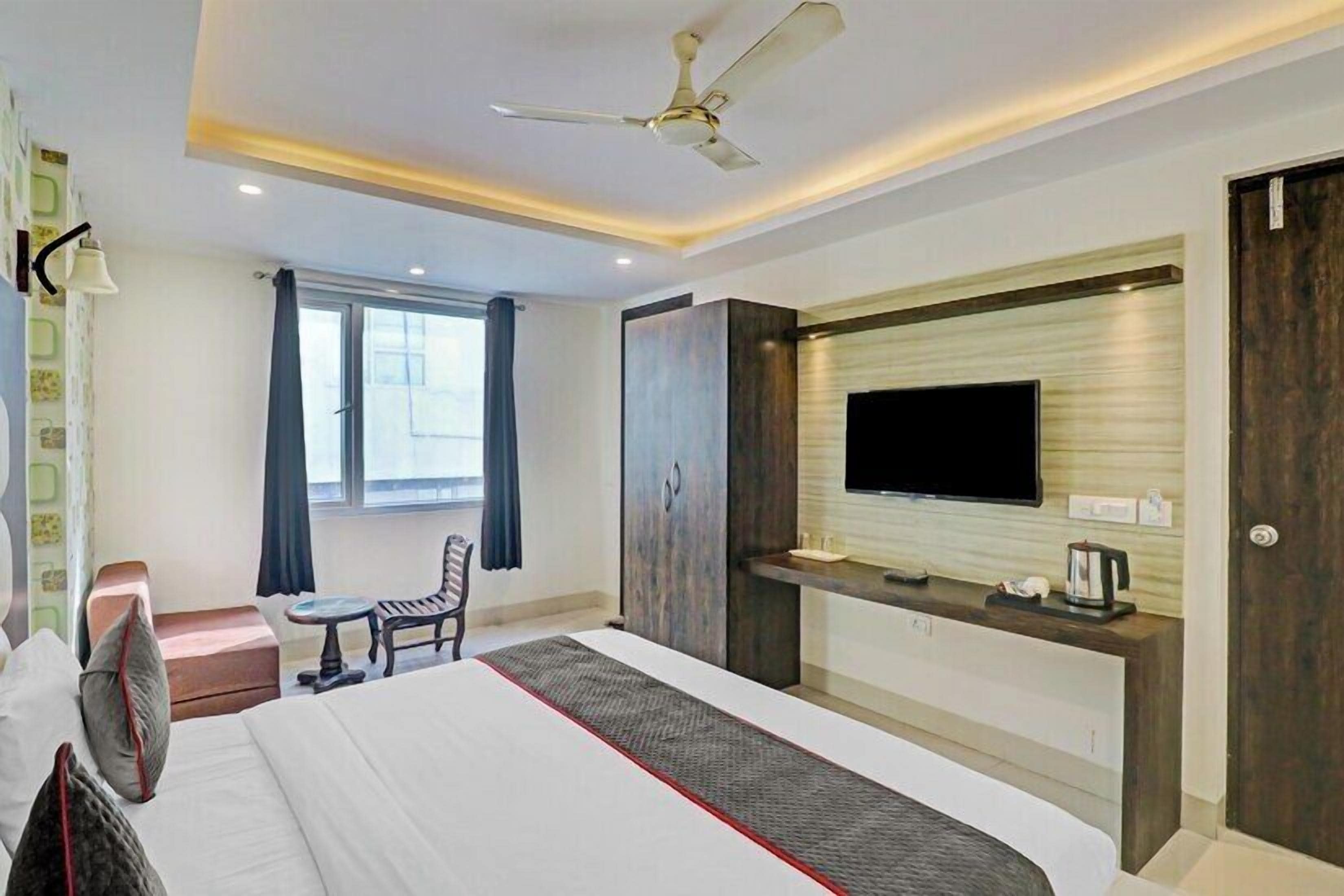 Habitación de hotel con cama, escritorio con televisor, silla, mesa pequeña y ventana con cortinas.