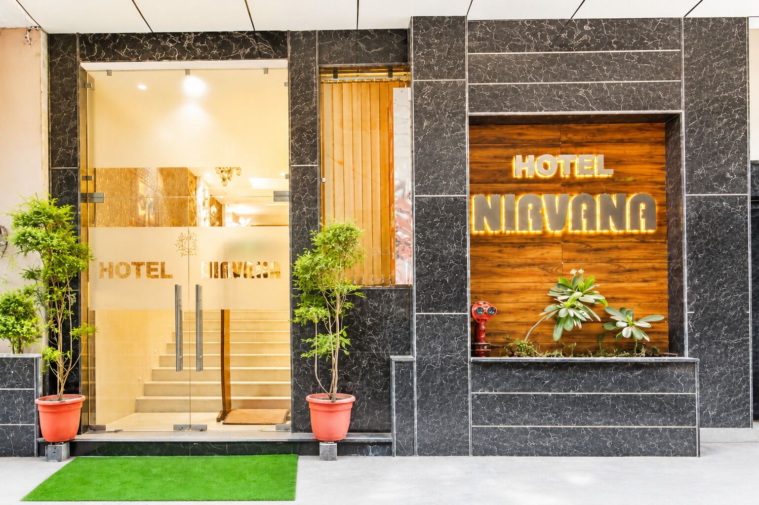 Ein Hotel mit Eingang, einer Glastür, einem Holzschild und Blumentöpfen.