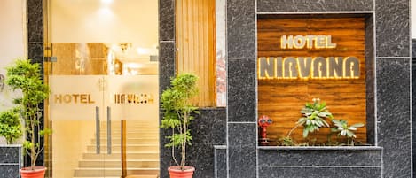 A hotel entrance with a glass door, a wooden signboard, and potted plants.