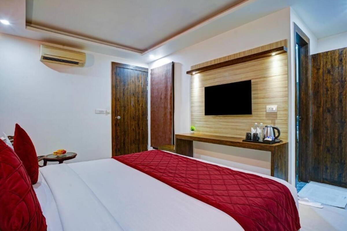 A hotel room with a bed, a TV mounted on the wall, a wooden panel wall, and a small table with a kettle.