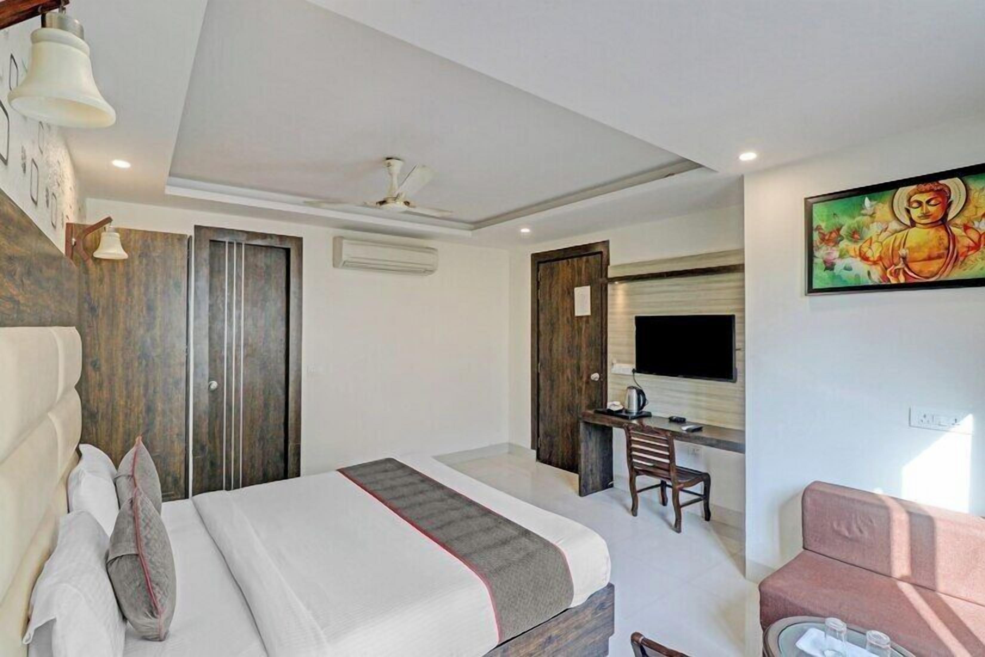 A hotel room with a bed, a desk, a chair, a TV, and a painting on the wall.