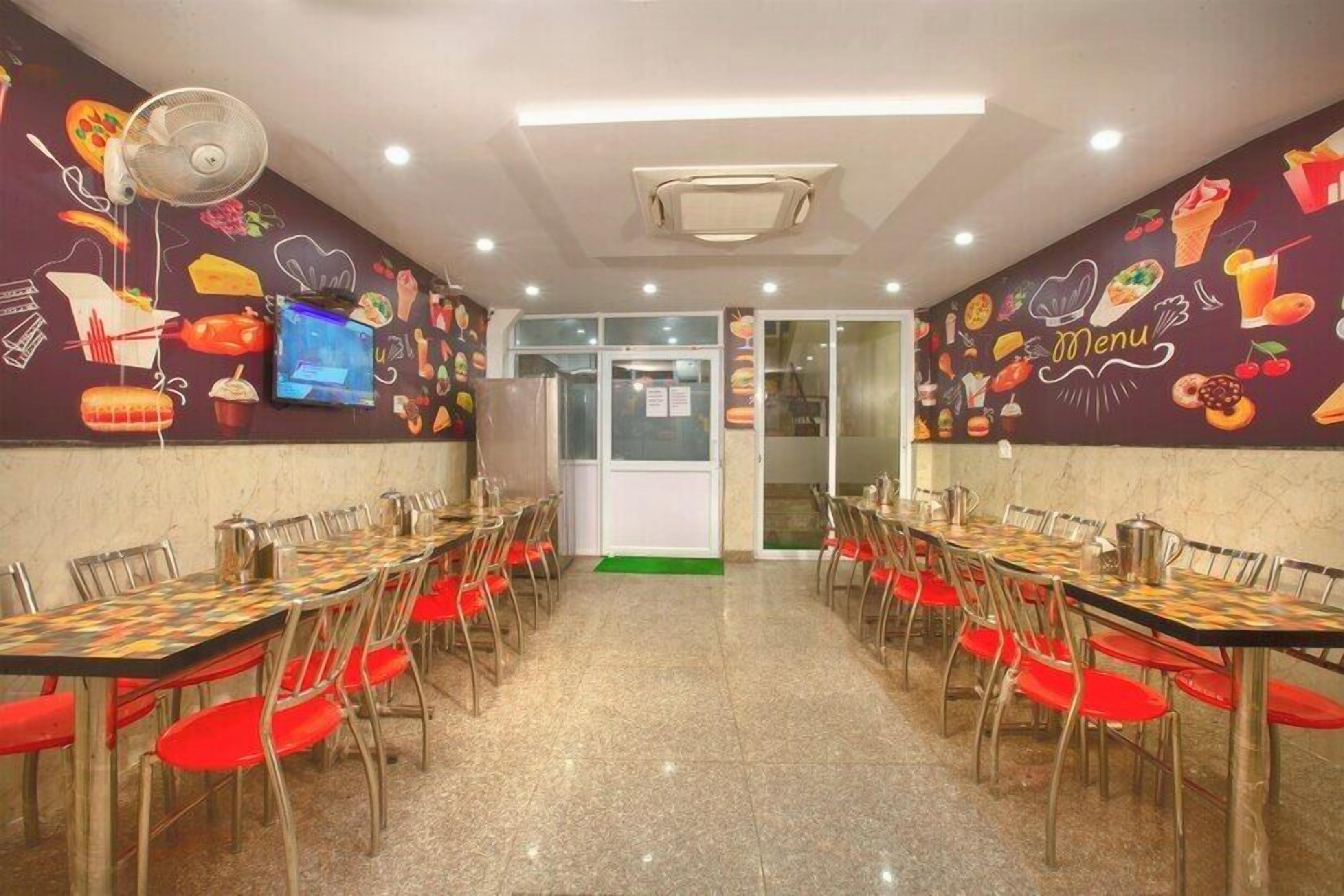 A restaurant with multiple tables and chairs, a television screen, and a menu wall.