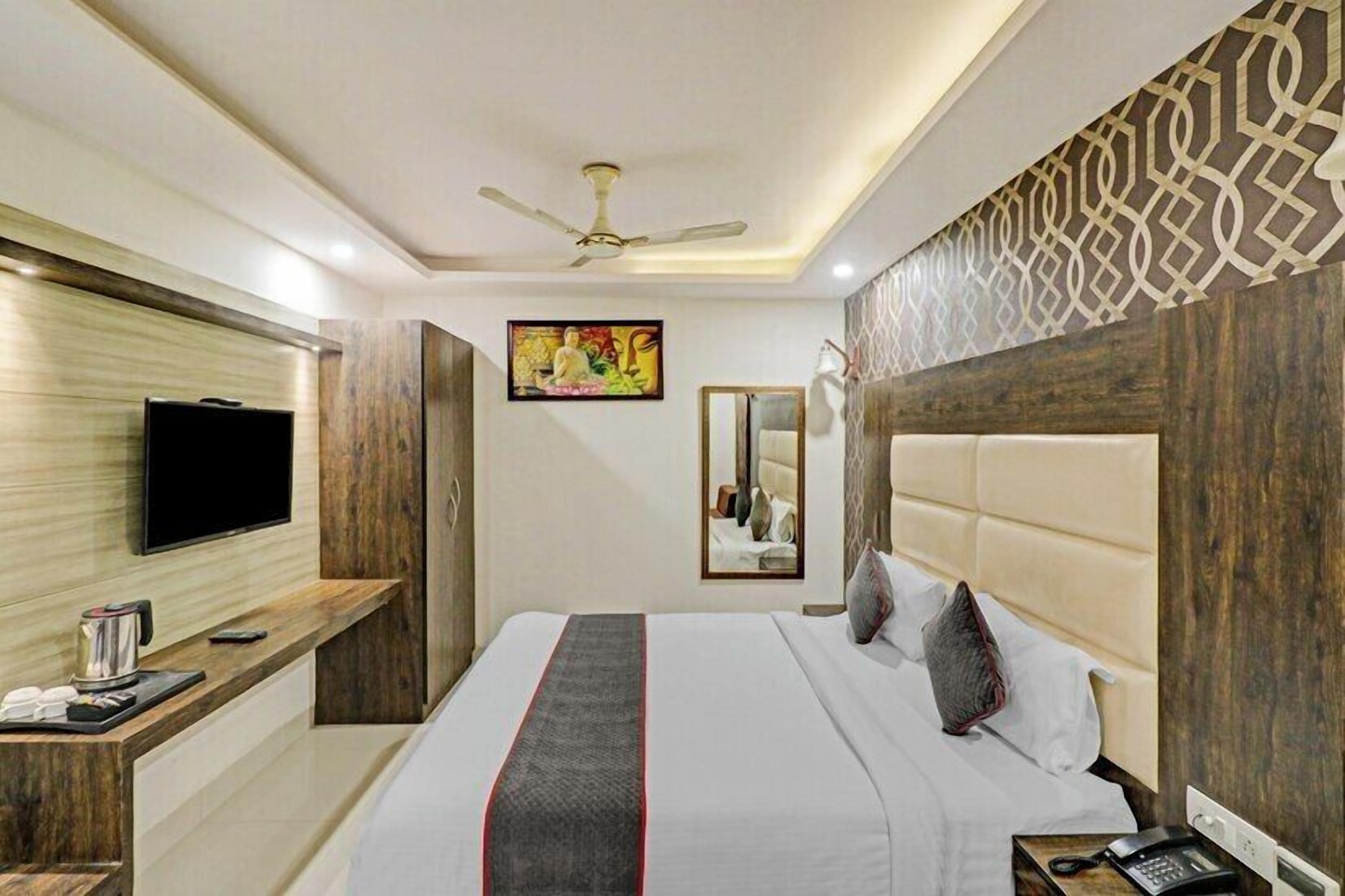 A hotel room with a bed, a television, a mirror, and a ceiling fan.