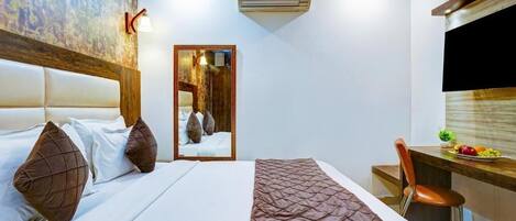 A hotel room with a bed, a desk, a chair, a mirror, and an air conditioning unit.