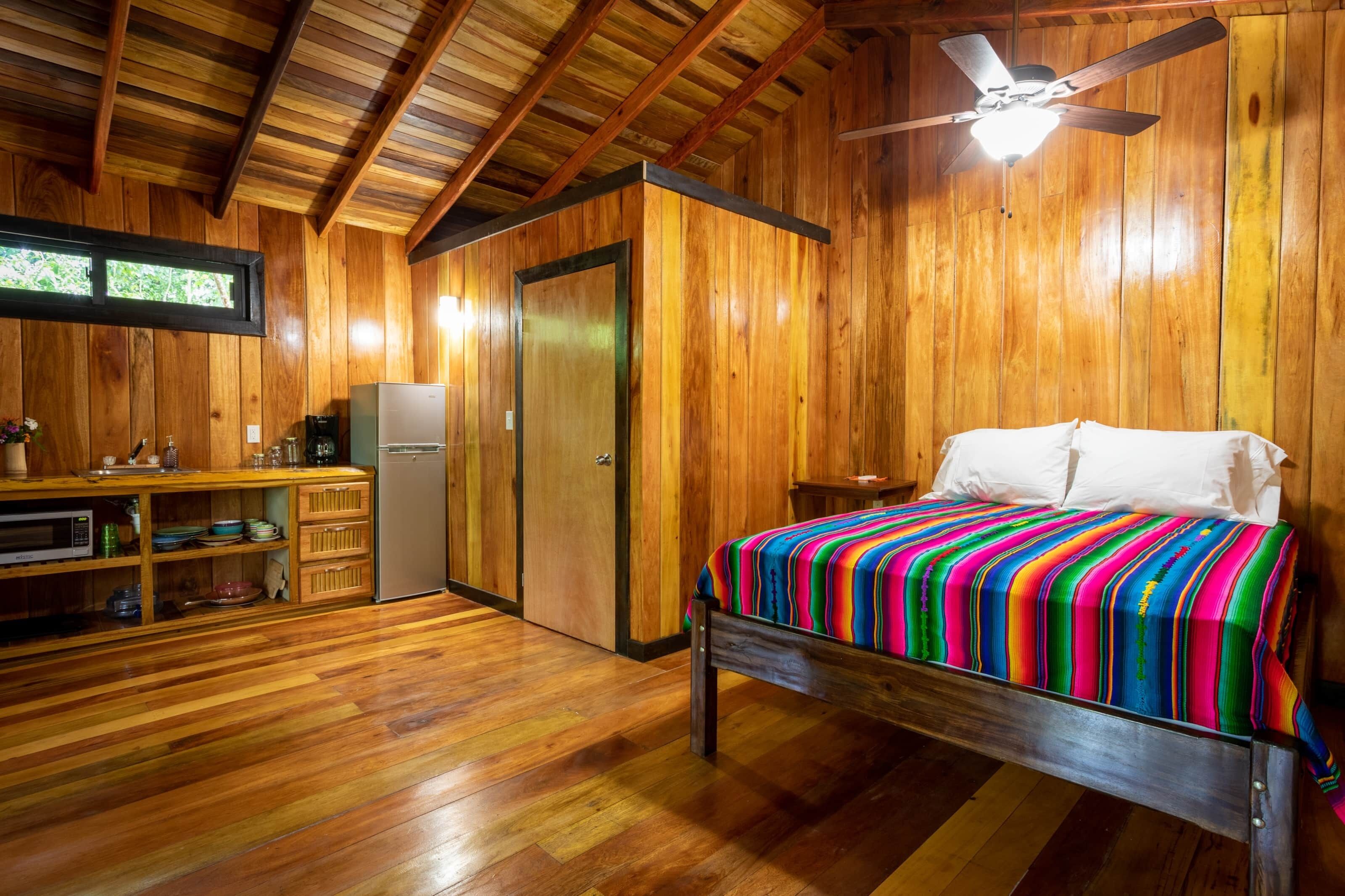 A wooden cabin with a bed, a desk, and a ceiling fan.